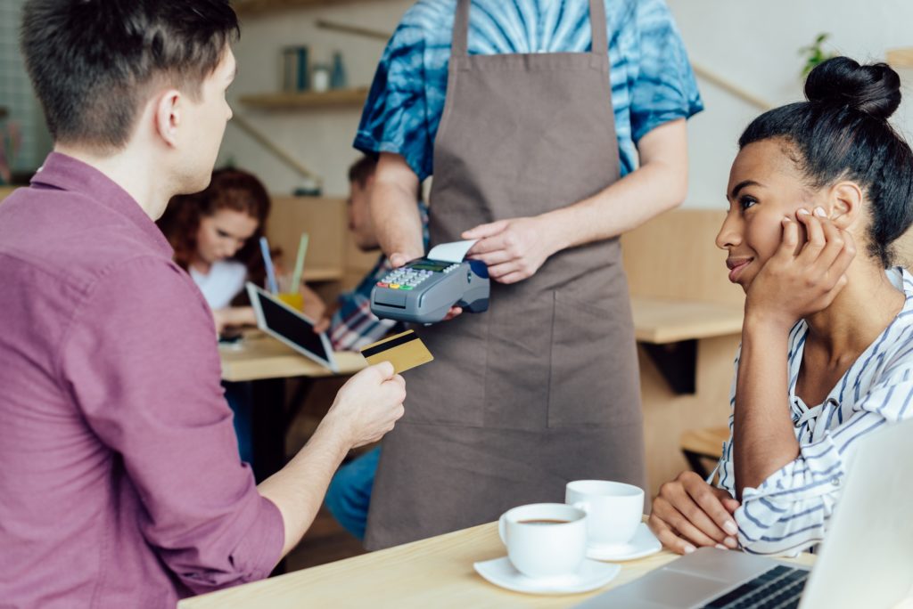 young multiethnic couple holding credit card while waiting receiving payment by mobile terminal